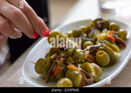 Hand of woman taking spicy skewered appetizers with green olives, anchovies and jalapeños. Traditional Basque gildas snack Stock Photo