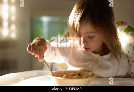 Small girl eats brakefast by herself with a spoon. Stock Photo