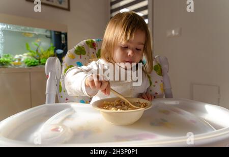 Small girl eats brakefast by herself with a spoon. Stock Photo