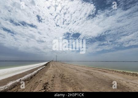 Salt lake and simple dirt road against a cloudy sky Stock Photo