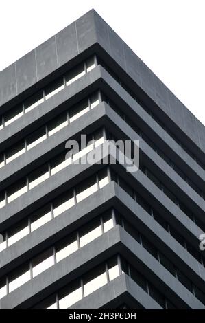 A corner detail of a typical brutalist style 1960s concrete office building with geometric concrete framework against a grey clo Stock Photo