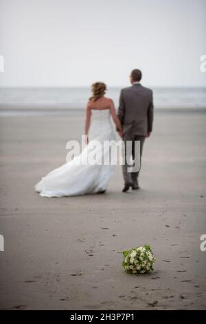 Out of focus and unrecognizable bride and groom walking away on the beach Stock Photo