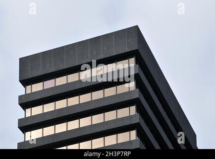 A corner detail of a typical brutalist style 1960s concrete office building with geometric concrete framework against a grey clo Stock Photo