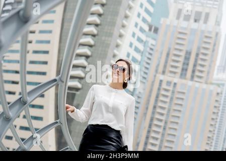 Beautiful businesswoman, smart dresses walking down the promenade in a big city. Stock Photo