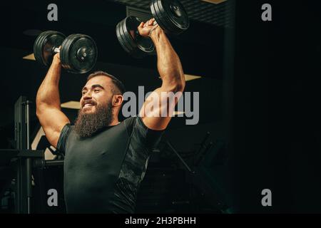 Bodybuilder doing exercises with dumbbells in a dark gym Stock Photo
