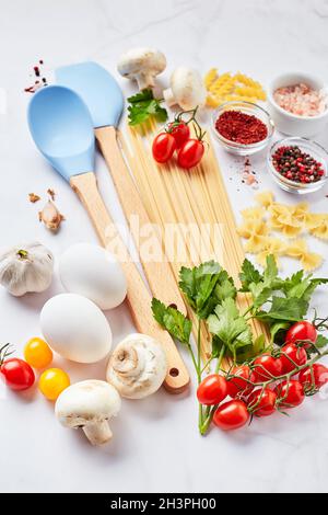 Food background with different kinds of pasta, tomatoes, herbs, mushrooms, eggs, seasonings scattered on light marble background Stock Photo