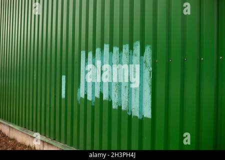 Fence painted after vandalism. Painting over graffiti on the fence. Blue paint on a green steel fence. Stock Photo