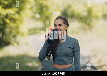 Tired runner woman jogger drinking bottled water after jogging in park outdoor.