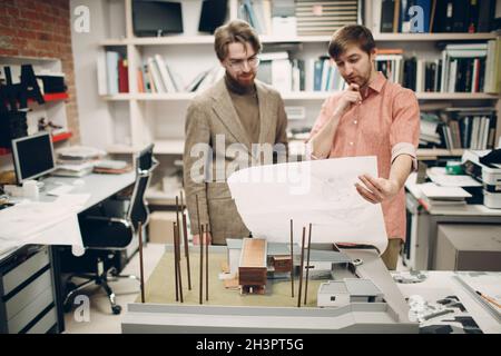 Young adult think architect working at the table with project, drawings blueprint and building layout at architectural bureau Stock Photo