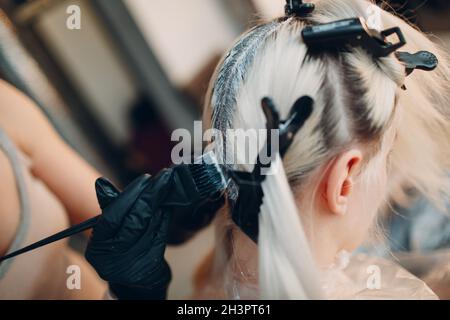 Young woman hairdresser dying hair at beauty salon. Professional hair roots coloring Stock Photo