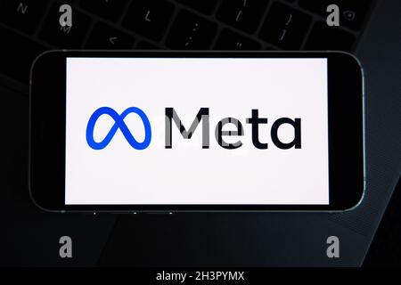 META company logo seen on smartphone in hand with Facebook logo on background screen. New Facebook company logotype for METAVERSE. Stock Photo