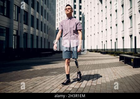 Disabled young man with foot prosthesis walks along the street Stock Photo