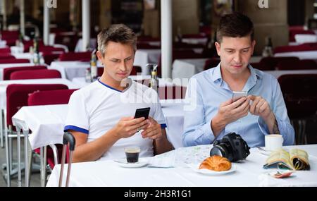 Two men sitting with coffee and looking at mobiles in cafe Stock Photo
