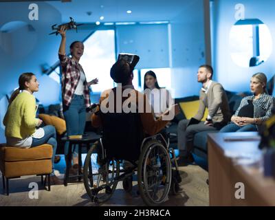 Disabled businessman in a wheelchair at work in modern open space coworking office with team using virtual reality googles drone Stock Photo