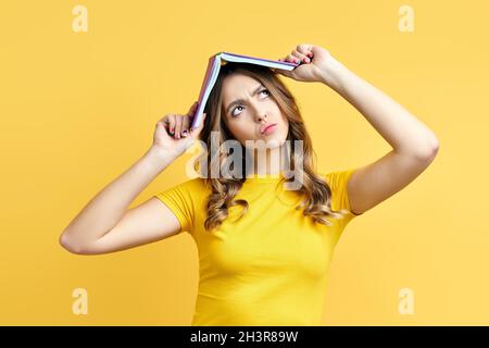 Photo of funny woman holding book over head, confused expression Stock Photo