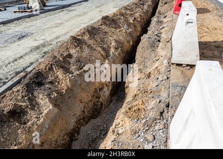 A narrow trench dug along the street on the sidewalk to repair the plumbing. Stock Photo