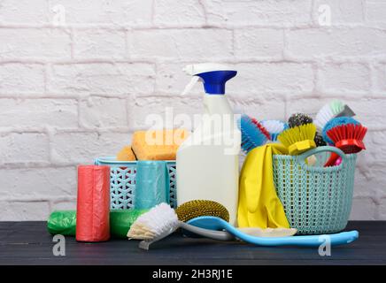 Sponges, plastic brushes and bottles of detergents on a blue wooden table. Household cleaning items on white brick wall backgrou Stock Photo