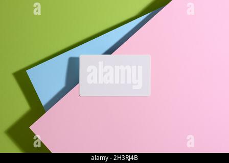 Blank rectangular business card lies on a modern bright green background with blue and pink sheets of paper with a shadow Stock Photo