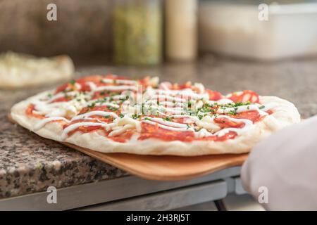 Pizza cook putting pizza in oven in a pizzeria, close up. Stock Photo