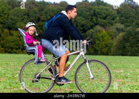 A little girl in child bike seat, man riding bike, child in bike seat, Toddler helmet Stock Photo