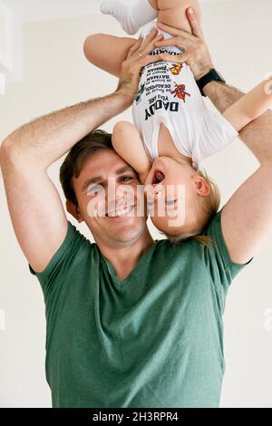 Smiling dad holds upside down little laughing girl Stock Photo