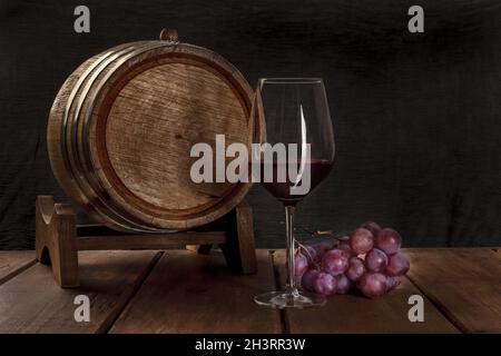 A glass of red wine with a wine barrel and grapes on a dark rustic background Stock Photo
