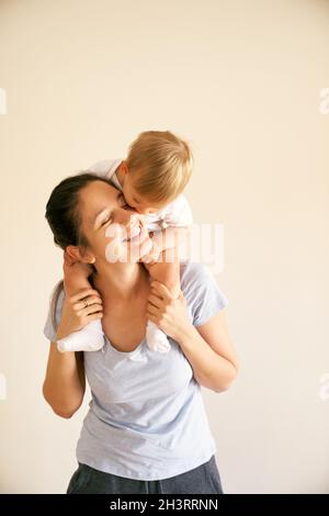 Smiling mother holds on her shoulders a little girl who kisses her. Portrait Stock Photo