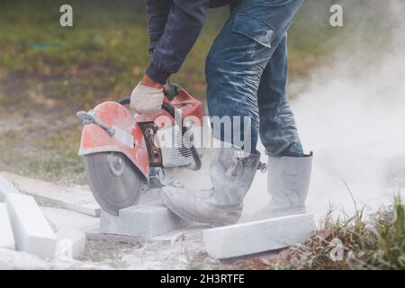Worker mason cuts the sidewalk tile with circular saw while repairing sidewalk in city street Stock Photo