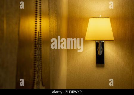 Modern sconce with turned on bulb under lampshade hanging on wall. Stock Photo