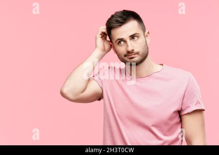 Young pensive man have doubts while scratching head looking to copy space on pink background Stock Photo