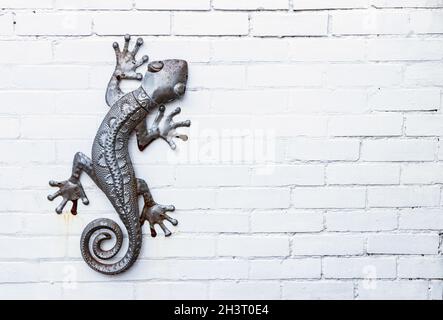 metal sculpture of a salamander gecko lizard isolated on white painted brick wall Stock Photo