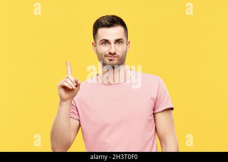 Young funny man pointing his finger up indicates to copy space isolated on yellow background Stock Photo