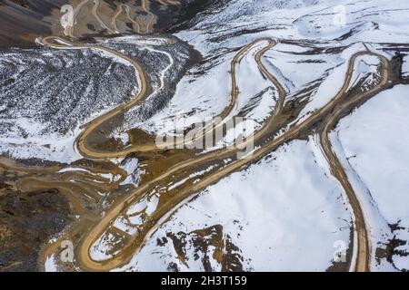 Aerial view of a winding dirt road cutting through a lush green forest ...
