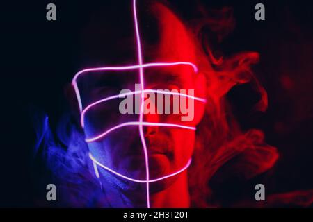 Portrait of man with neon glow tube lines with smoke on his face in dark. Concept cyberpunk and virtual reality. Stock Photo