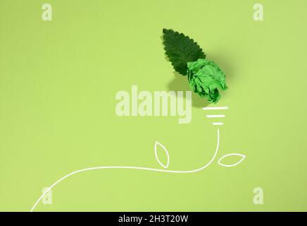 A crumpled sheet of paper and a green leaf on a green background, the shape of a light bulb. Energy saving concept, new creative Stock Photo