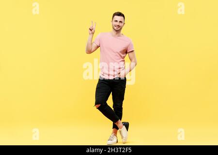Full length portrait of trendy handsome man show victory sign on yellow background Stock Photo