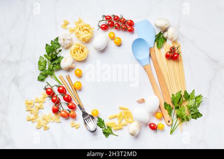 Food background with place for text, with different kinds of pasta, tomatoes, herbs, mushrooms, eggs, seasonings scattered on li Stock Photo