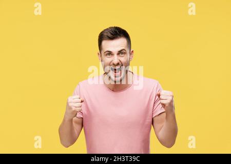 Young man celebrating with winner gesture on yellow background Stock Photo