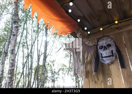 halloween decorations with ghost and a huge skeleton head on a wooden wall with birch trees in the background Stock Photo