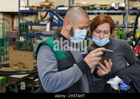 Industrial workers with face masks protected against corona virus discussing about production in factory. People working during Stock Photo