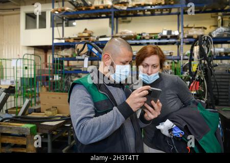 Industrial workers with face masks protected against corona virus discussing about production in factory. People working during Stock Photo