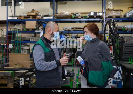 Industrial workers with face masks protected against corona virus discussing about production in factory. People working during Stock Photo