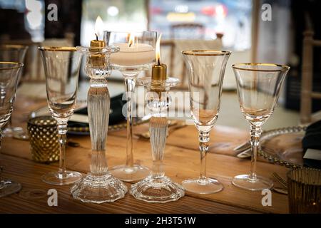 Empty crystal glass wine glasses & candlesticks lit on wooden table, part of a wedding table setting display at weddings fair in Wadebridge, Cornwall Stock Photo