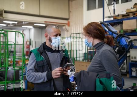 Industrial workers with face masks protected against corona virus discussing about production in factory. People working during Stock Photo