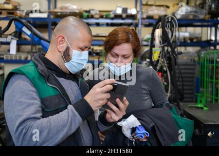 Industrial workers with face masks protected against corona virus discussing about production in factory. People working during Stock Photo