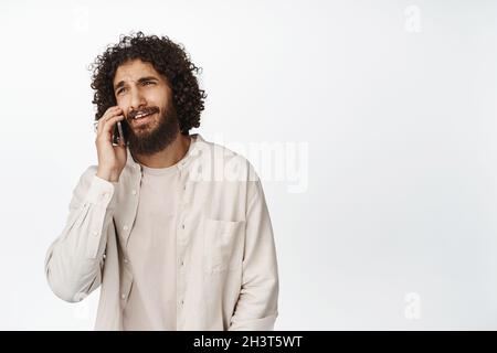 Smiling handsome middle eastern guy talking on mobile phone, having a call, standing over white background Stock Photo