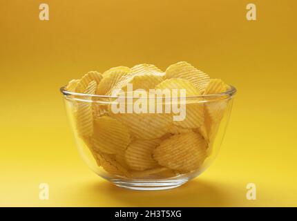 Ridged potato chips in bowl on yellow background Stock Photo