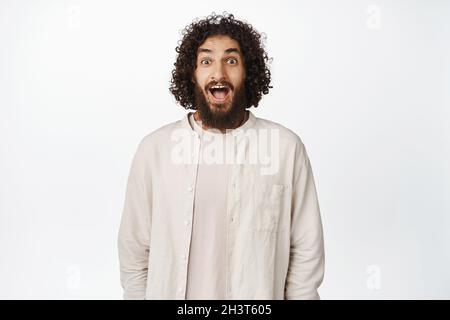 Portrait of surprised and excited middle eastern man, drop jaw and gasping in awe, looking at something amazing, white background Stock Photo