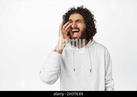 Portrait of arab man screaming, searching and calling for someone, shouting and making announcement, standing over white background Stock Photo