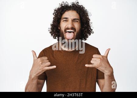 Portrait of carefree middle eastern man showing tongue and yolo gesture, having fun, enjoying party, looking cool and happy, white background Stock Photo